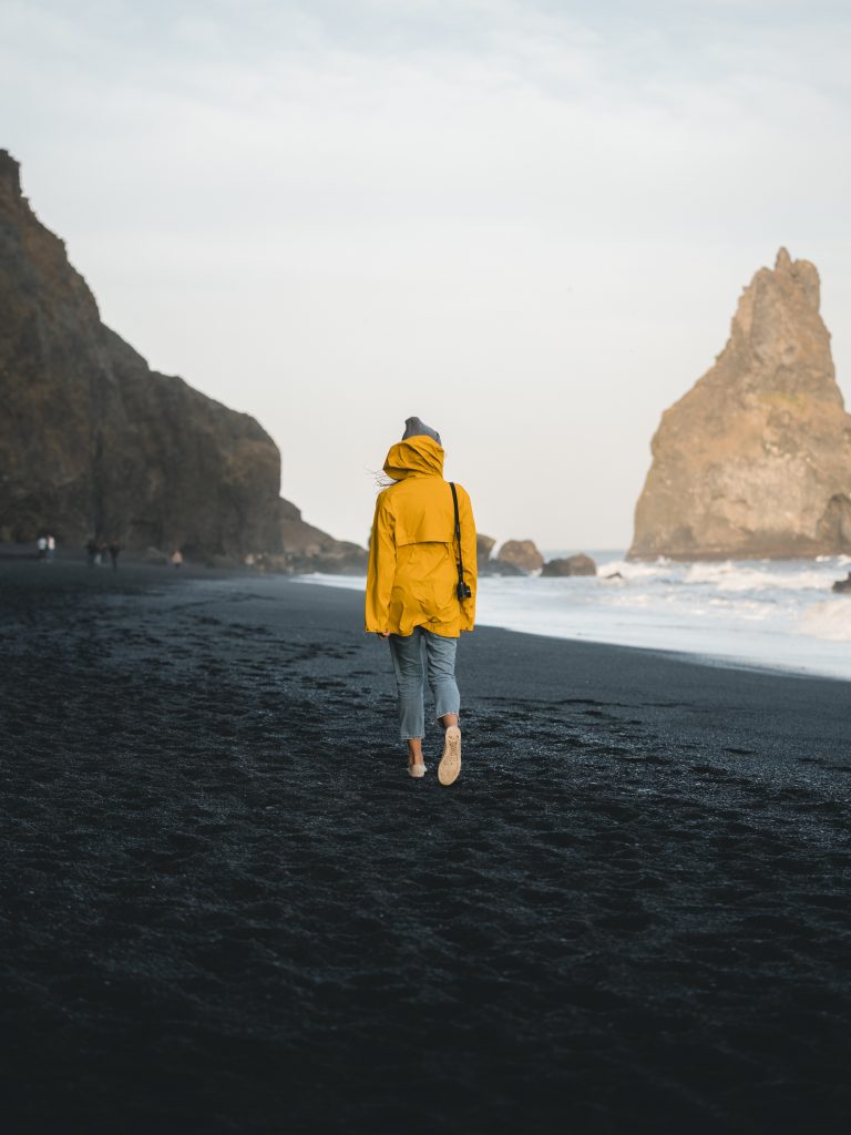 Frau im gelben Regenmantel am Strand in Iceland