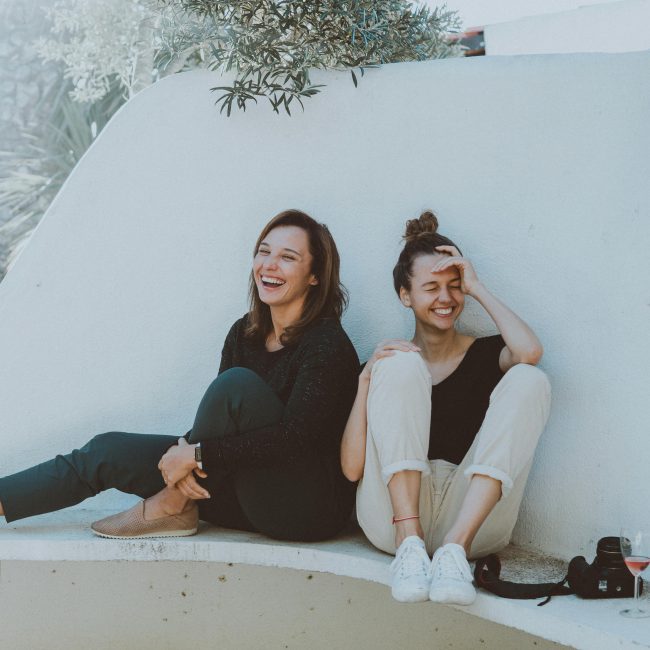 Zwei junge Frauen sitzen auf weißen Steinbank und lachen