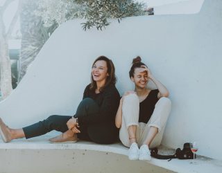 Zwei junge Frauen sitzen auf weißen Steinbank und lachen