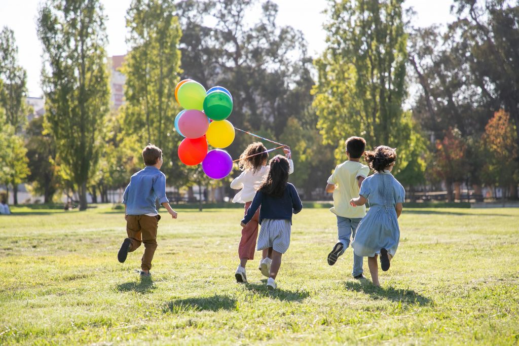 Kinder rennen auf der Wiese mit Ballons