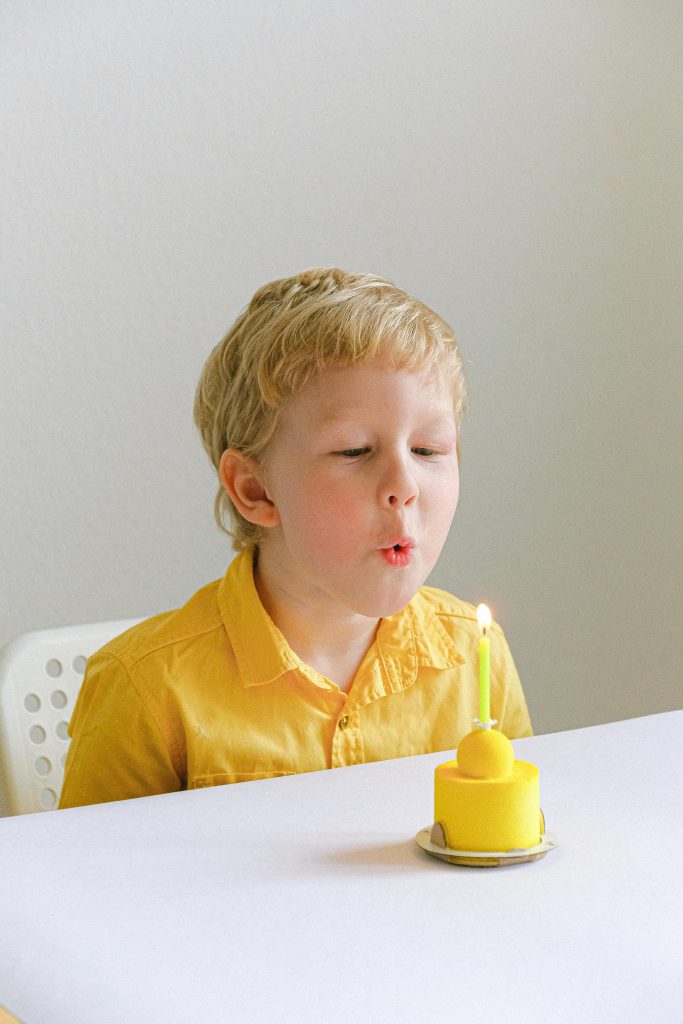 Kleiner Junge im gelben Poloshirt pustet eine Geburtstagskerze vom gelben Muffin